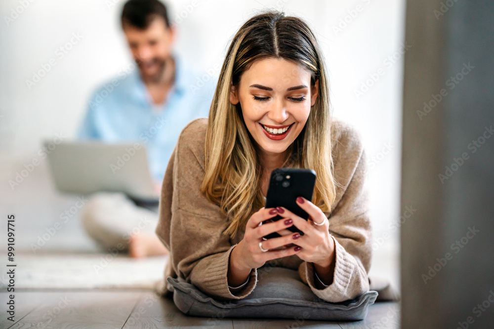 Happy smiling young woman holding smartphone on floor at home using online entertainment mobile app Happy smiling young woman holding smartphone on floor at home using online entertainment mobile app