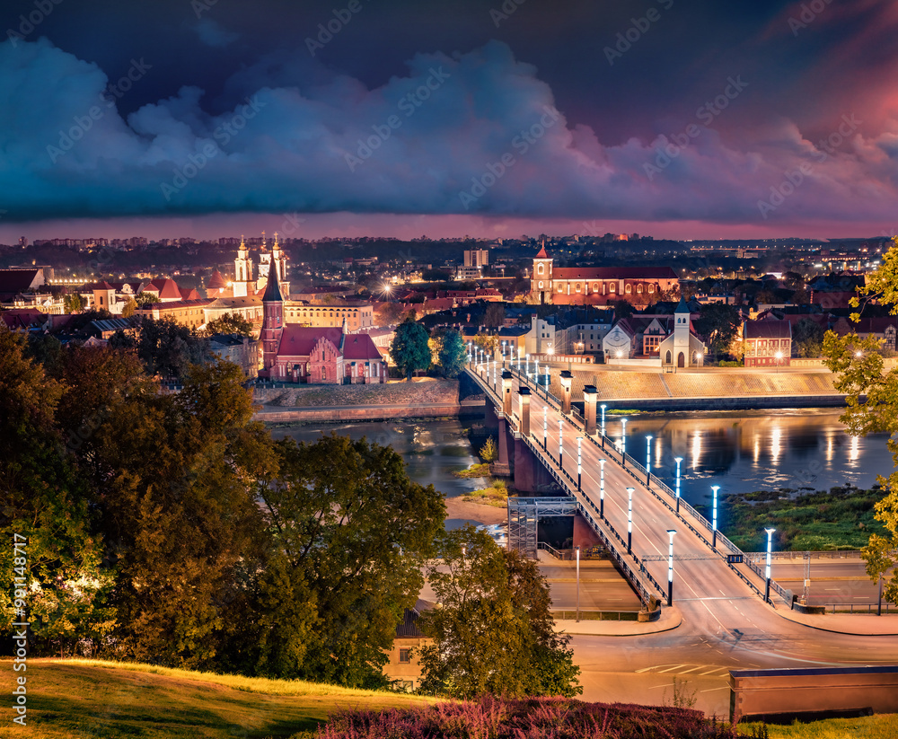 Night autumn cityscape of Kaunas town with Church of Vytautas the Great on background. Illuminated morning view of Vytautas the Great Bridge over Nemunas river, Lithuania, Europe. Travel the world..