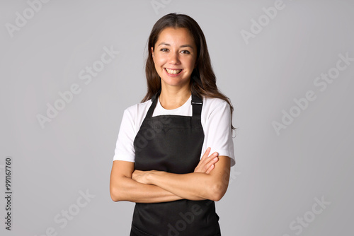 Portrait of young woman in black apron standing with arms crossed. Woman wearing apron and white shirt, white background