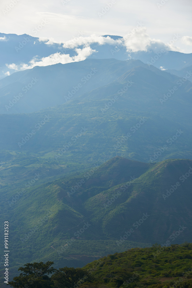 Colombian Andean landscape, layers of mountains covered with lush, green vegetation and a sky with sun and clouds. View from a lookout point in Guane, Santander.