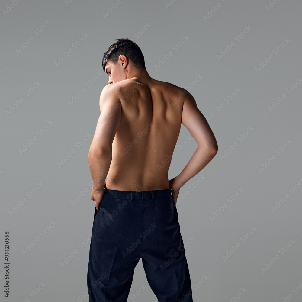 Fototapeta premium Back view of shirtless man with relief, strong, muscular body, back, posing in pants isolated on grey studio background. Concept of male beauty, body and skin care, health, sport