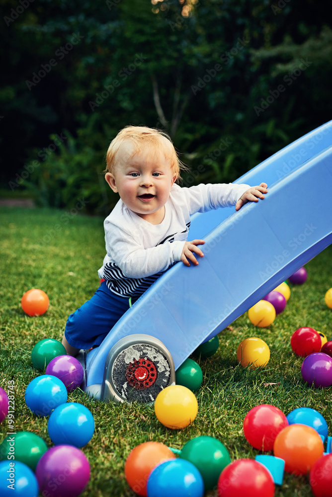 Obraz premium Game, colourful balls and baby in backyard, relax and playful with fun, happiness and calm. Smile, infant and toddler on grass, cheerful and carefree with motor skills, kid and childhood with nature