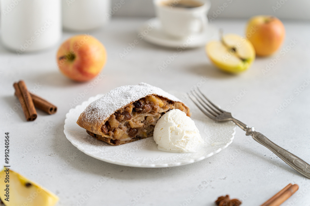 Freshly baked powdered apple strudel with raisins and ice cream on white plate with red apples and cinnamon on white background. homemade Apfelstrudel, austrian germany cuisine. Menu, recipe Freshly baked powdered apple strudel with raisins and ice cream on white plate with red apples and cinnamon on white background. homemade Apfelstrudel, austrian germany cuisine. Menu, recipe