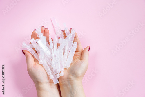Medical eye drops in plastic pipettes on pink background. Pile of empty plastic ampoules for drops in hands. Plastic vials of saline solution