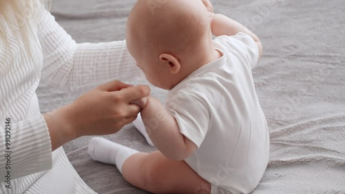 Mother and baby perform simple exercises to strengthen baby's neck, back and stomach muscles. Mom helps her newborn baby sit up for first time by doing exercises while holding hands. 