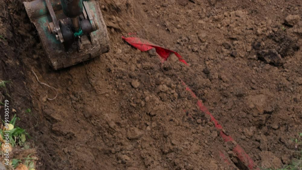 A mini digger is actively engaged in excavating soil in a residential backyard, preparing the area for landscaping improvements. The machine removes dirt and debris, showcasing efficient digging techn
