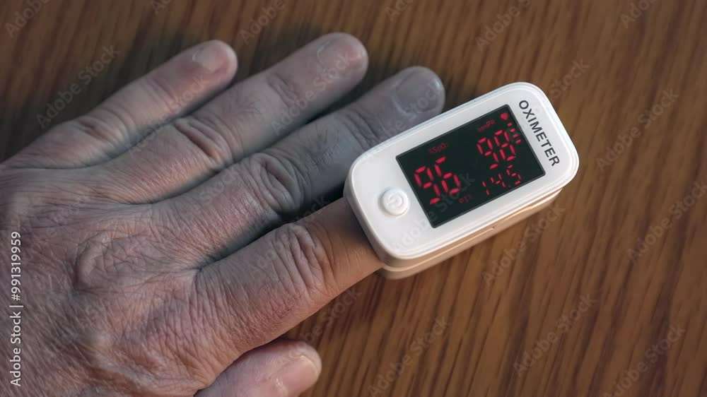 A person is using a fingertip pulse oximeter to measure their blood oxygen levels. The device displays readings on a small screen while resting on a wooden surface. A person is using a fingertip pulse oximeter to measure their blood oxygen levels. The device displays readings on a small screen while resting on a wooden surface.