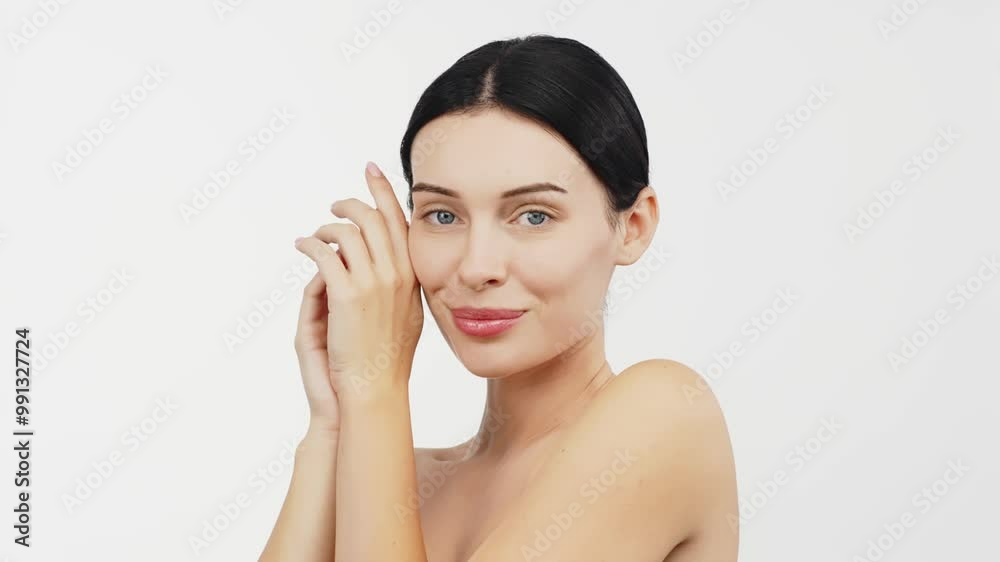 A young woman in a studio against a white background gently touches her flawless skin. Her expression conveys joy and harmony, highlighting her allure and well-groomed appearance. A young woman in a studio against a white background gently touches her flawless skin. Her expression conveys joy and harmony, highlighting her allure and well-groomed appearance.