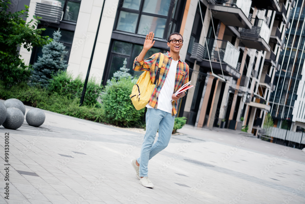 Full length portrait of nice young man walk wave hi wear plaid shirt buildings downtown street outdoors Full length portrait of nice young man walk wave hi wear plaid shirt buildings downtown street outdoors