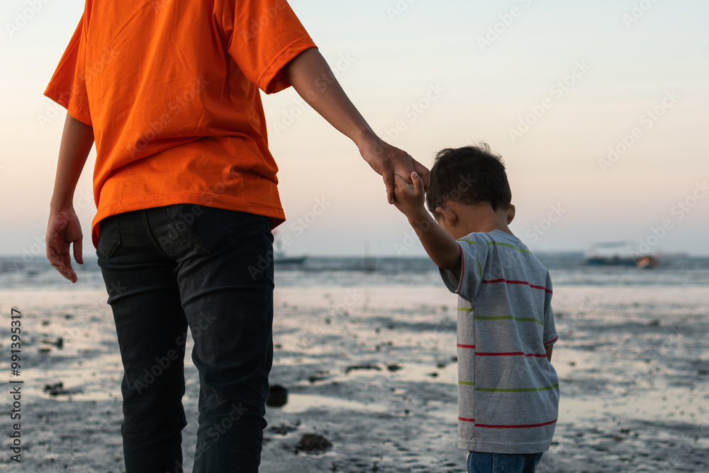 a mother holding her son's hand heading towards the beach a mother holding her son's hand heading towards the beach
