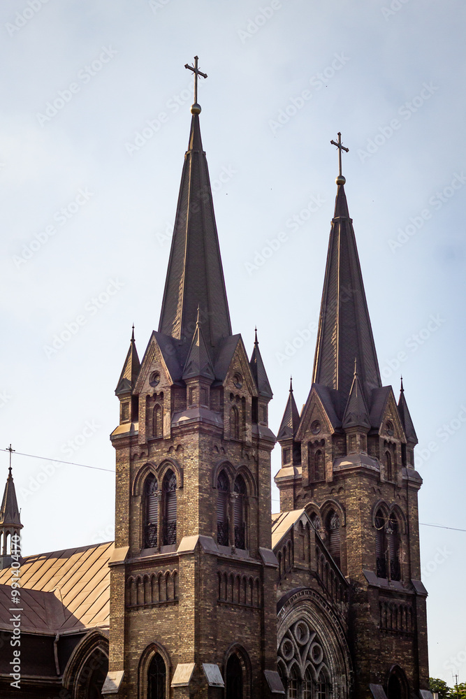 Obraz premium City building landscape, Gothic church towers and spiers, arched windows of a stone building. Color vertical photo from the side of the church facade.