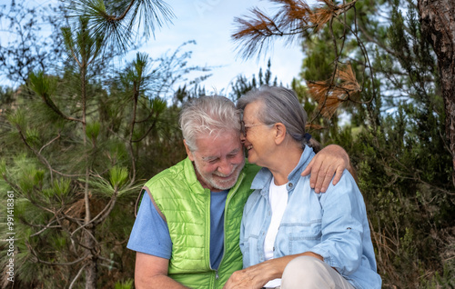 Tender senior couple sitting outdoors in the woods hugging exchanging cuddles. Two mature people enjoying nature and healthy lifestyle in retirement