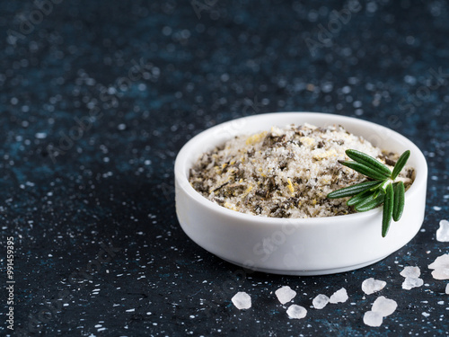 Sea salt scented herb rosemary and lemon zest. Sea salt with aromatic herbin small bowl on dark blue background. Scented salt and ingerdients. Copy space photo