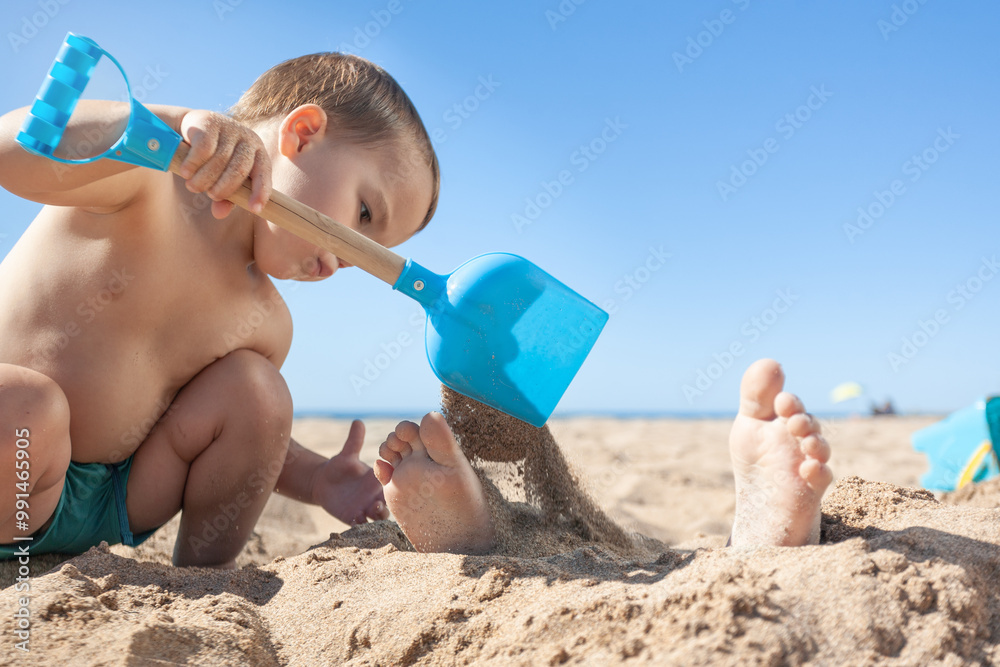 Toddler throws sand on his brother's feet with a shovel Toddler throws sand on his brother's feet with a shovel