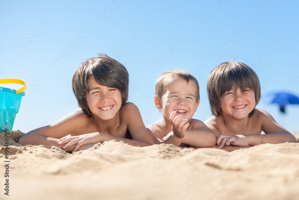 Three boys are laying on the beach, smiling and enjoying the sun Three boys are laying on the beach, smiling and enjoying the sun