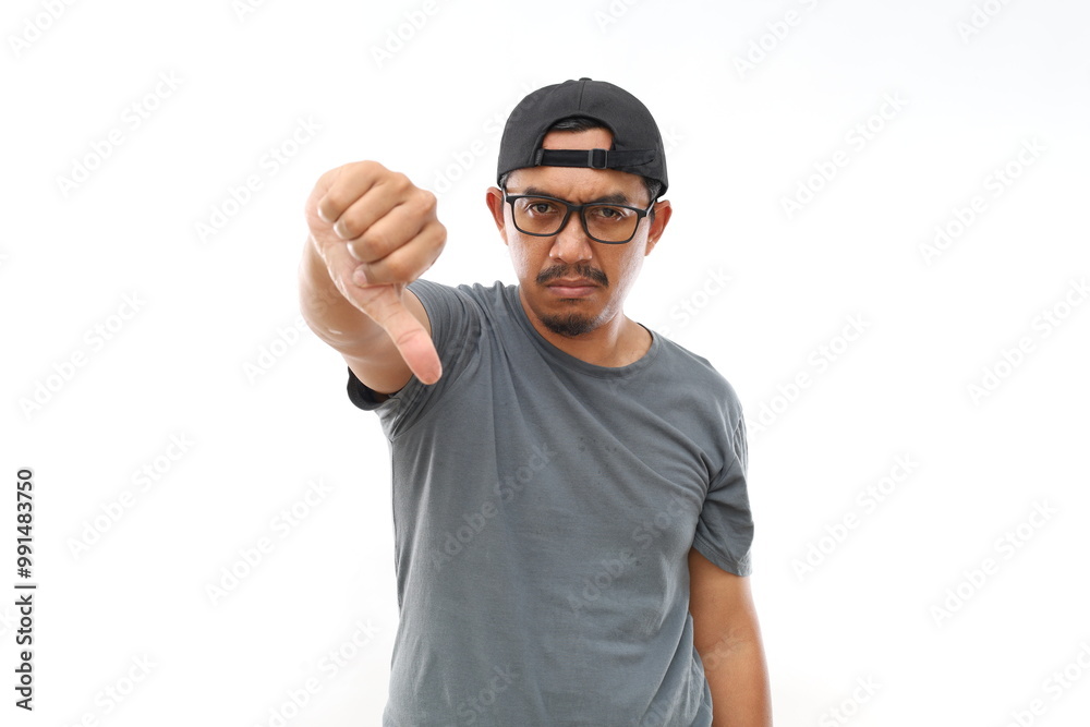 Naklejka premium Asian man with beard wearing casual t-shirt and glasses looking unhappy and angry showing rejection and negative with thumbs down gesture. Bad expression.