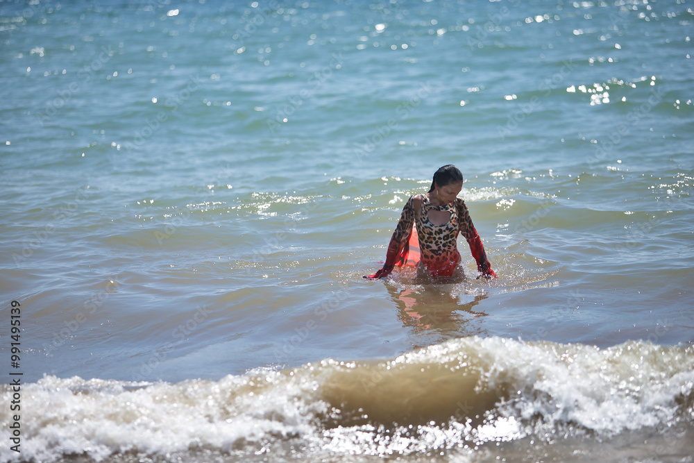 Young woman, beautiful, brunette, with a leopard swimsuit and sarong, totally wet posing in the water on the shore of the beach with the sea in the background. Concept beauty, fashion, femininity. Young woman, beautiful, brunette, with a leopard swimsuit and sarong, totally wet posing in the water on the shore of the beach with the sea in the background. Concept beauty, fashion, femininity.