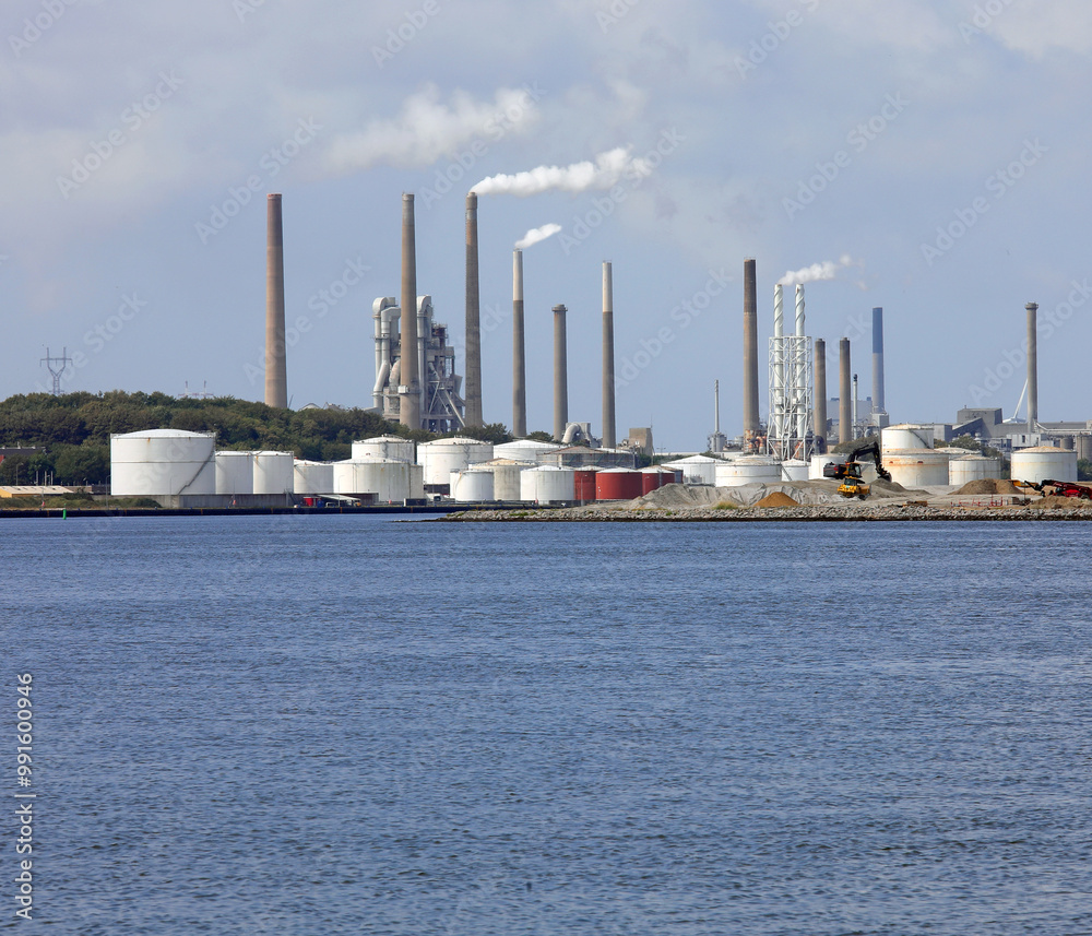 Obraz premium Wide modern cement factory with chimneys puffing out white smoke and the seaside during the production