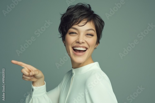 A smiling Asian woman points to the side against a clean white background, showcasing her natural beauty and genuine expression. 