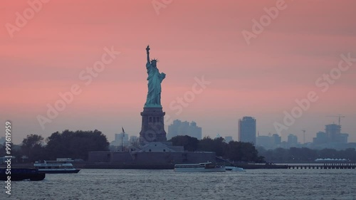 The majestic view of the Statue of Liberty from the boat at vibrant pink sunset. Visiting New York City and sightseeing. Downtown Manhattan and NYC skyline in the background. 