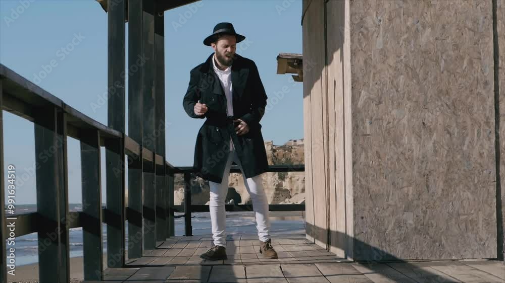 An elegant man with a hat dances joyfully on his balcony, enjoying the music and the stunning sea view, radiating positivity and carefree spirit.