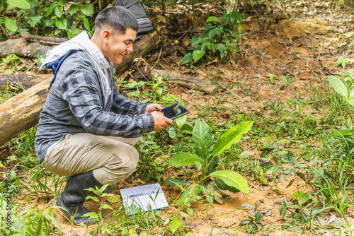  A biologist takes a photo of a growing plant with a tablet in the middle of the jungle