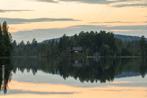 A typical Swedish stuga among the trees by the lake. Sweden is the land of lakes, trees, and the typical Swedish red cottages, also known as stuga. The veil of clouds creates soft light. photo