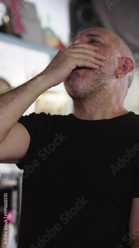 Vertical, a bald man yawns in a pub, showing a mix of fatigue and relief after a long day. The scene captures his need for rest and the comfort of the pub. photo