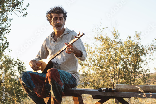 Man playing kopuz at sunset in an olive field photo