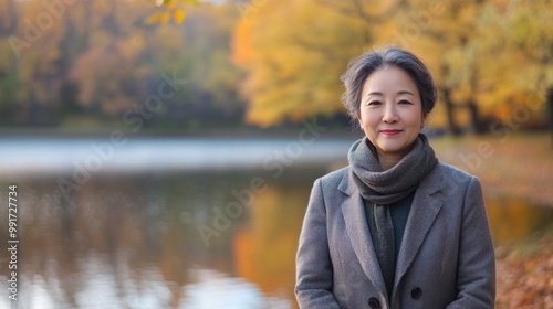 A woman stands by the lakeside surrounded by vibrant autumn leaves. Warm sunlight filters through the trees, highlighting her peaceful expression as she embraces the beauty of the season.