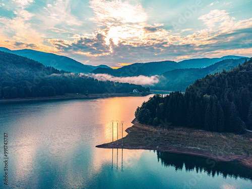 Stunning drone shot of a mountain lake reflecting the warm hues of sunset, surrounded by towering peaks.