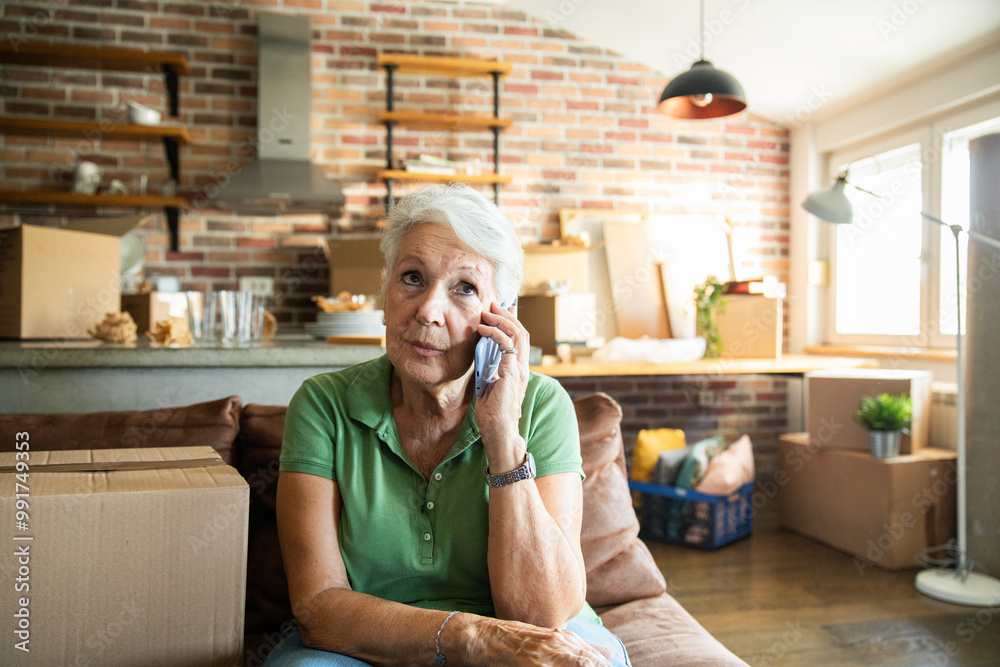 Senior woman on phone while labeling moving boxes in new home Senior woman on phone while labeling moving boxes in new home