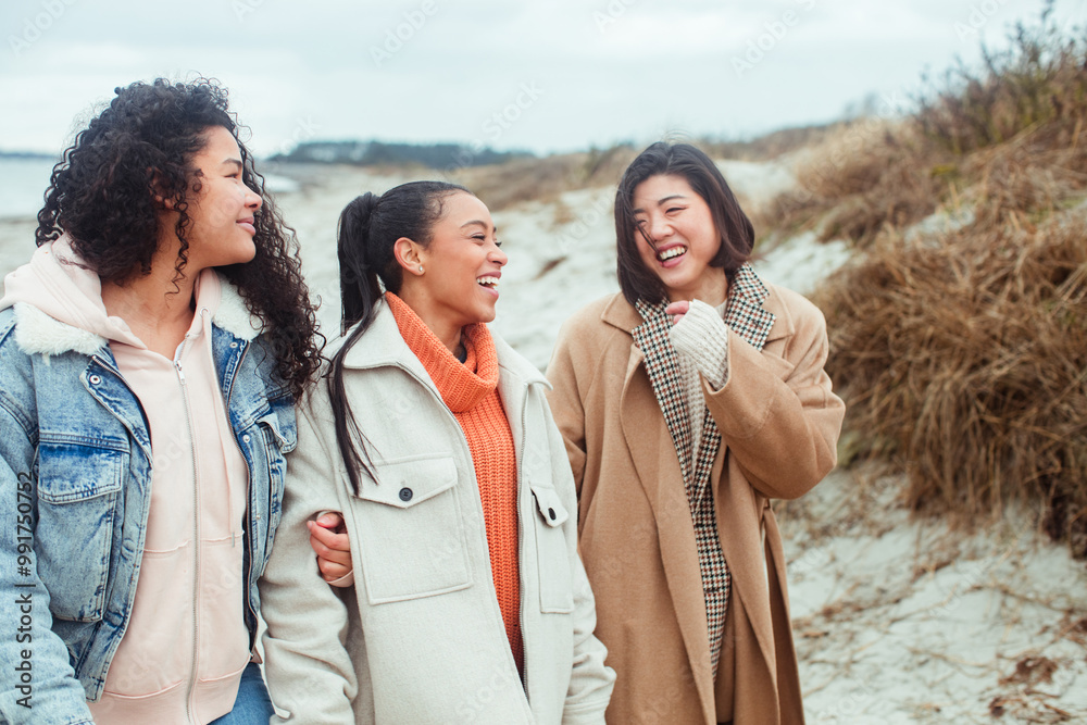 Three diverse young female friends walking on the beach in winter Three diverse young female friends walking on the beach in winter