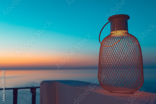 Close up shot of a led light lantern resting on a restaurant wall above the sea, at sunset, in a mediterranean island. Magic, romantic atmosphere, pink sky, orange soft led light.