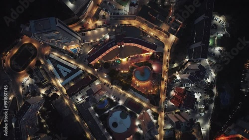 Top down aerial view of modern city at night. Birds eye overhead shot of apartmentbuildings with pools, streets and city traffic. Night life with street lights in the city.  photo