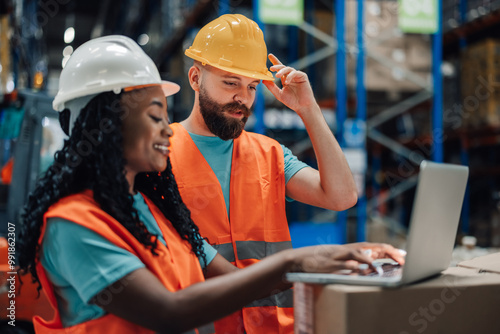 Multiracial man and woman collaborating on laptop for warehouse tasks