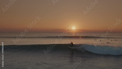 Surfers riding blue ocean waves at golden sunset in Portugal. Surfers in the sea at the popular surf spot in golden light. Fun sport activity in the sea. Slowmotion view of a male surfer surfing on th
