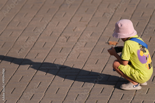 teenage boy in bright clothes on the street squatting and looking at smartphone