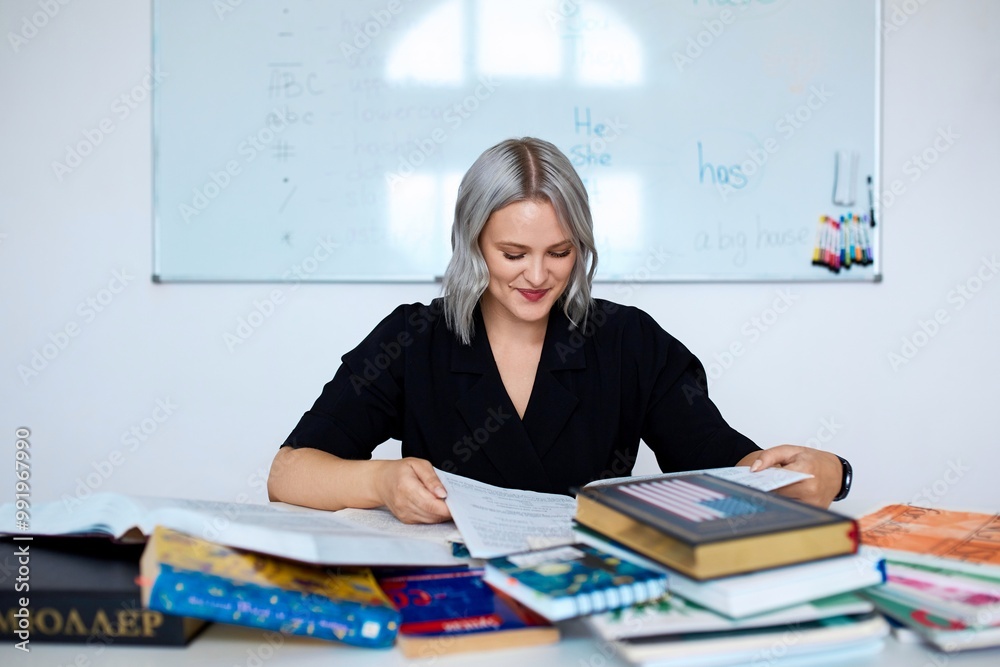 Portrait of a young beautiful English teacher working at school, at her desk with a bunch of books. Portrait of a young beautiful English teacher working at school, at her desk with a bunch of books.