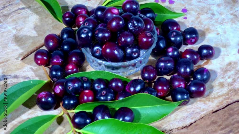 A bowl of java plums surrounded by java plum leafs on a rotating table A bowl of java plums surrounded by java plum leafs on a rotating table