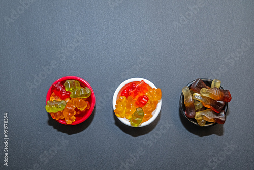 Colourful and small gel candies in small bowls. Grey ground and background. Top view. photo