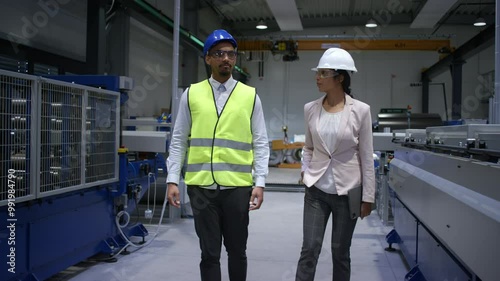 Indian female factory manager introducing the production line to a recruit, an African American worker, and congratulating him on a new job, front view.