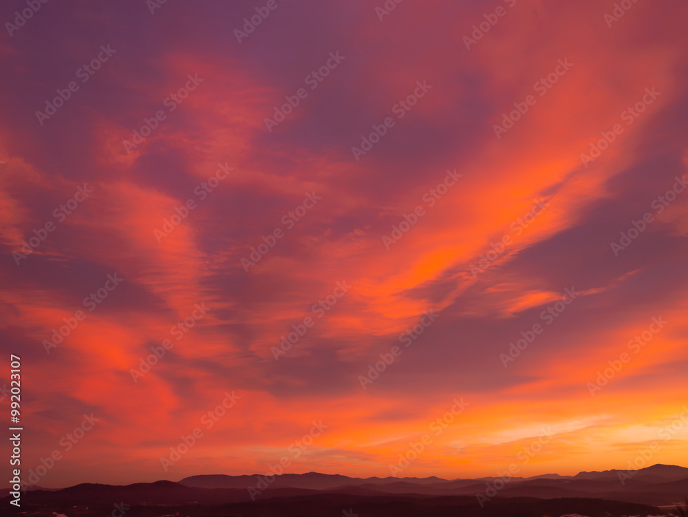 Fototapeta premium Expansive sky with a palette of orange and pink hues as sun sets behind distant mountain horizon. Tranquil beauty of nature at twilight, with vibrant sky contrasting against darkening land below.