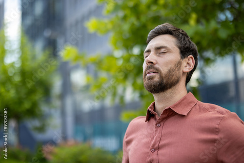 Mature male professional standing outside in city with eyes closed, experiencing calm and relaxation. Businessman taking break, capturing serene and positive emotions in urban setting a