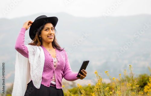 Foto de una feliz y bonita campesina con un sombrero hablando por un teléfono celular en los Andes peruanos. Mujer usando teléfono móvil