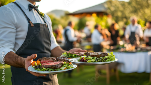 A serving staff carrying white plates with steak and salad outdoor wedding party.