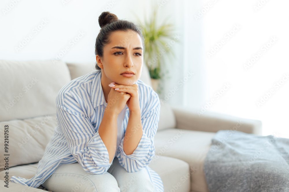 Upset arabian or indian young woman in casual clothes, sitting on a sofa in a living room, feeling sad tired and loneliness, suffering depression, worried about personal troubles or divorce, offended Upset arabian or indian young woman in casual clothes, sitting on a sofa in a living room, feeling sad tired and loneliness, suffering depression, worried about personal troubles or divorce, offended