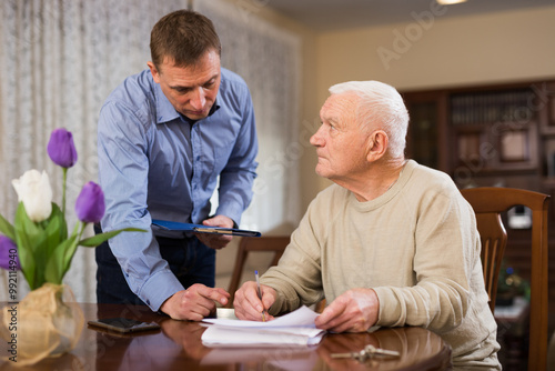 Troubled senior man discussing documents with his adult son while sitting at home table photo