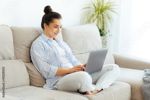 Online work. Happy pretty indian or arabian brunette woman in casual wear, sitting on a comfortable sofa at home in living room, using her laptop for distant work on a project, smiling