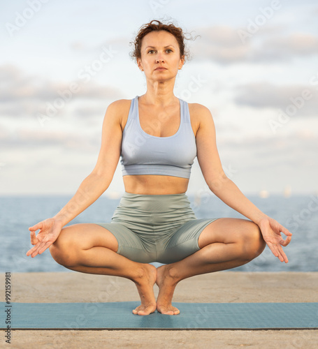 Woman practicing hatha yoga on sea beach, stretching in an asymmetrical seated asana Parivritta Janu Sirsasana photo